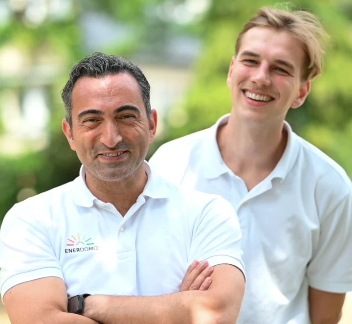 Zwei lächelnde Männer im weißen Polohemd von Enerdomo stehen im Grünen zusammen.