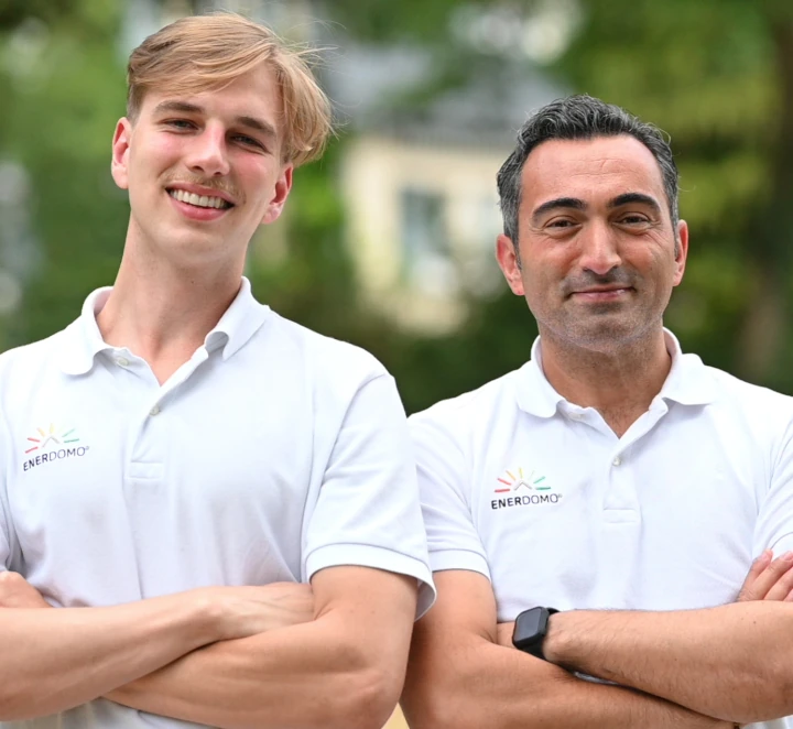 Zwei ENERDOMO-Mitarbeiter stehen lächelnd im Freien mit weißen Firmen-Poloshirts.