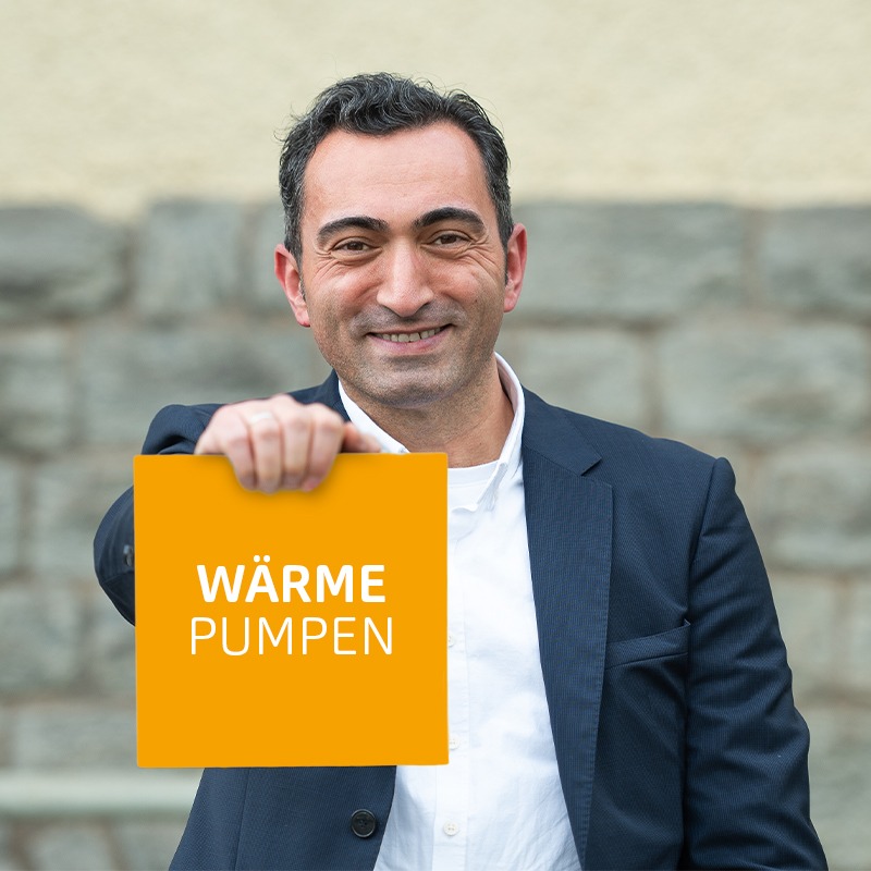 Ein Mann im Anzug hält ein Schild mit der Aufschrift „Wärmepumpen“ lächelnd hoch.